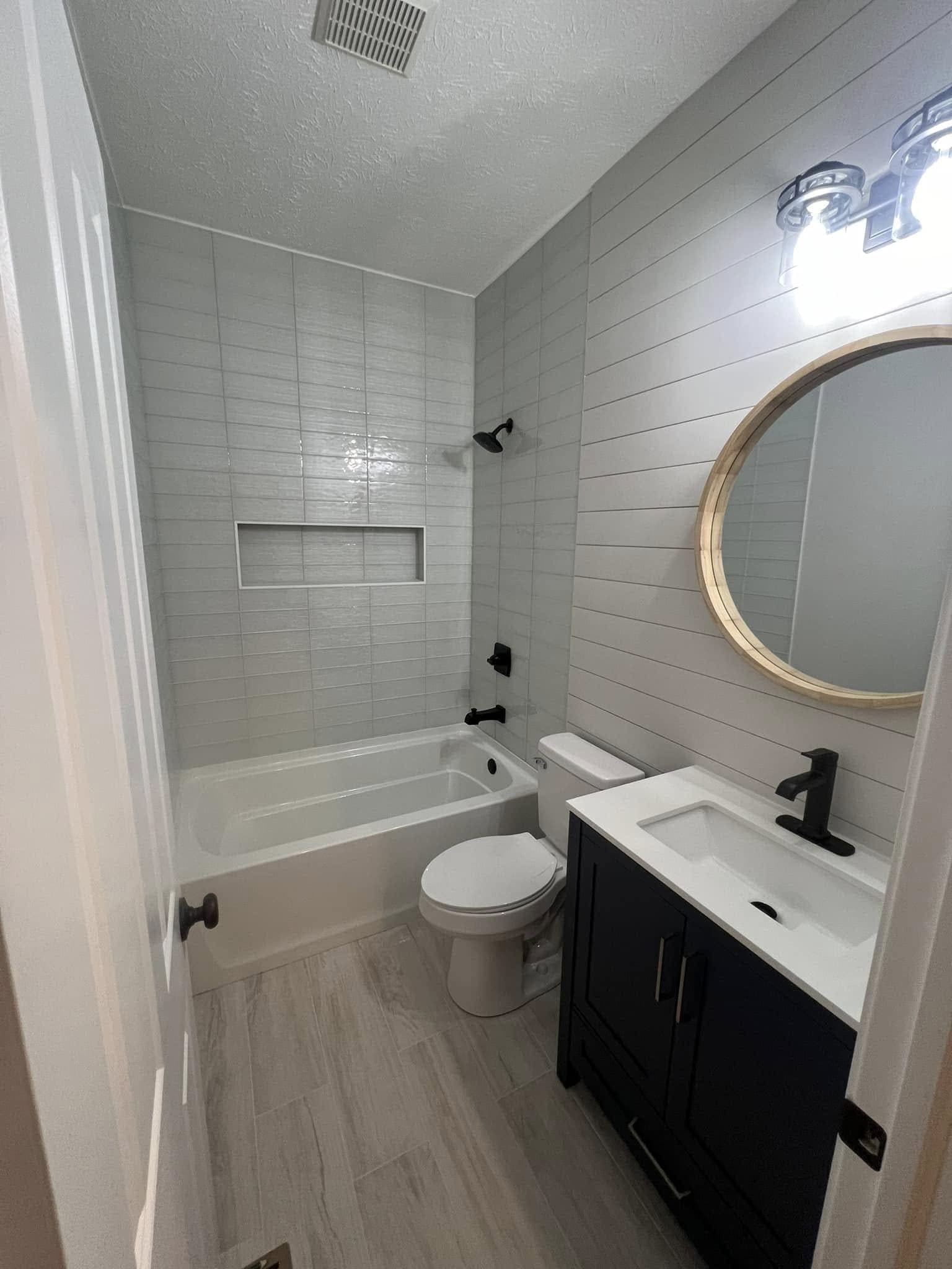 Bathroom with a shiplap wall, a tiled tub surround and a navy vanity