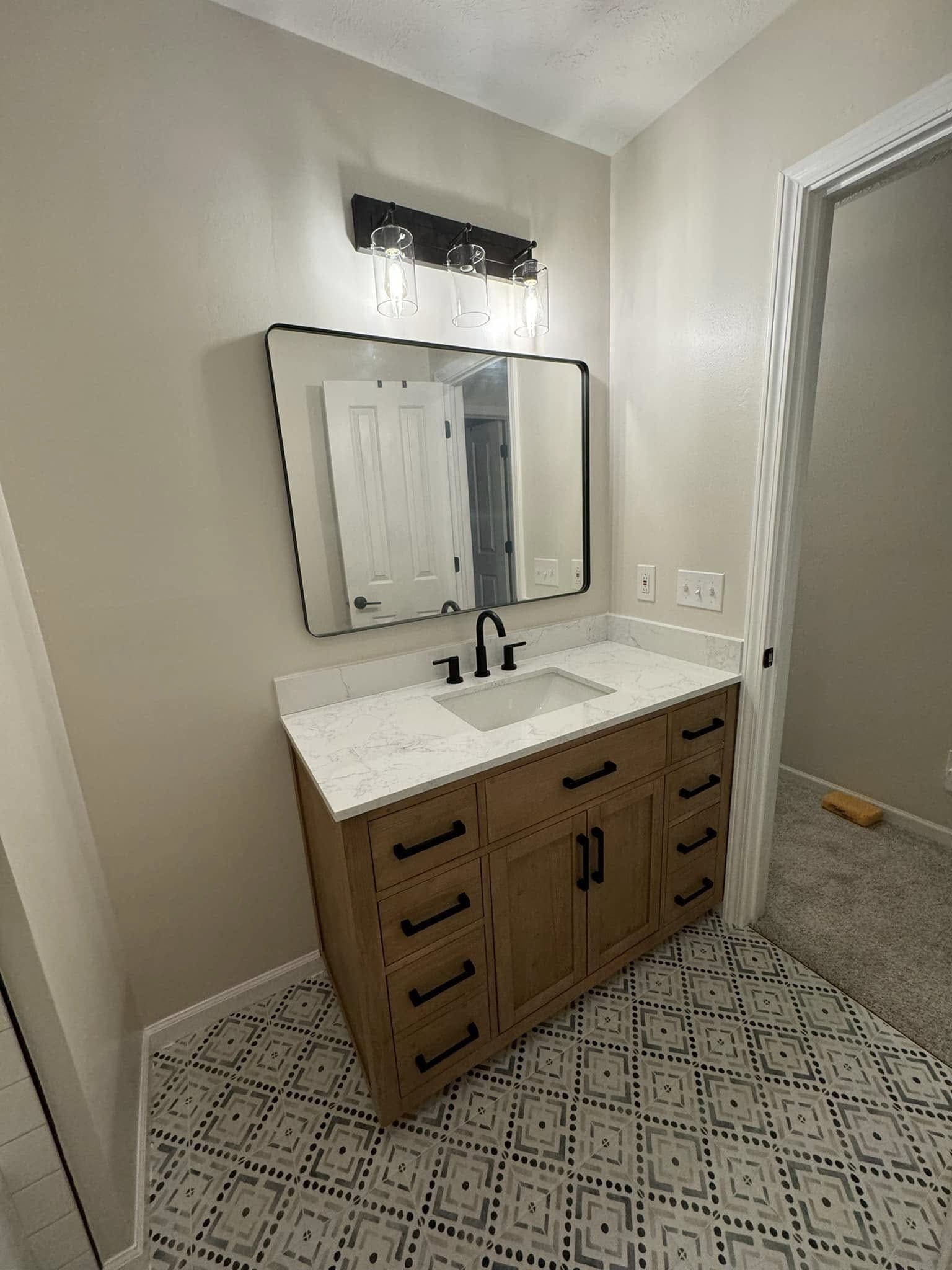 Bathroom vanity in wood with a marble-look top, black fixtures and patterned floor tile