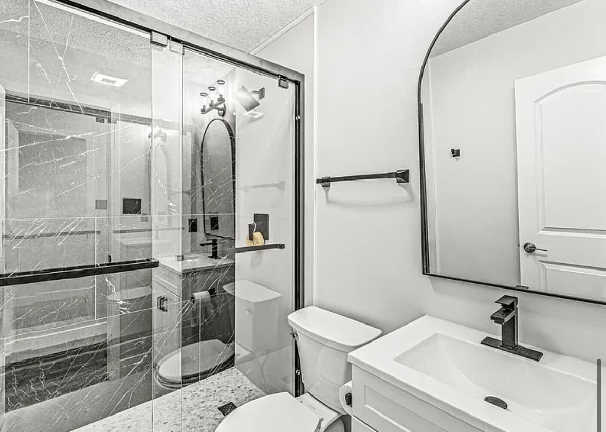 Finished bathroom with a glass shower, marble-look tiled walls and an arched mirror over the vanity