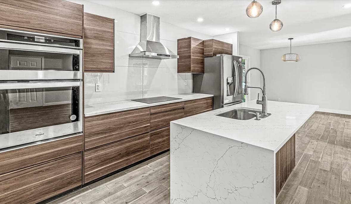 Kitchen with walnut cabinets, built-in wall ovens and a waterfall quartz island