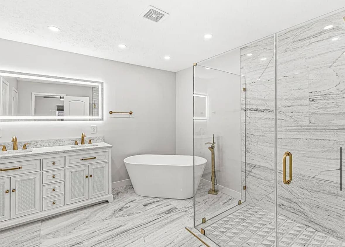 Marble bathroom with a freestanding tub, a glass shower, a lit mirror and brass fixtures
