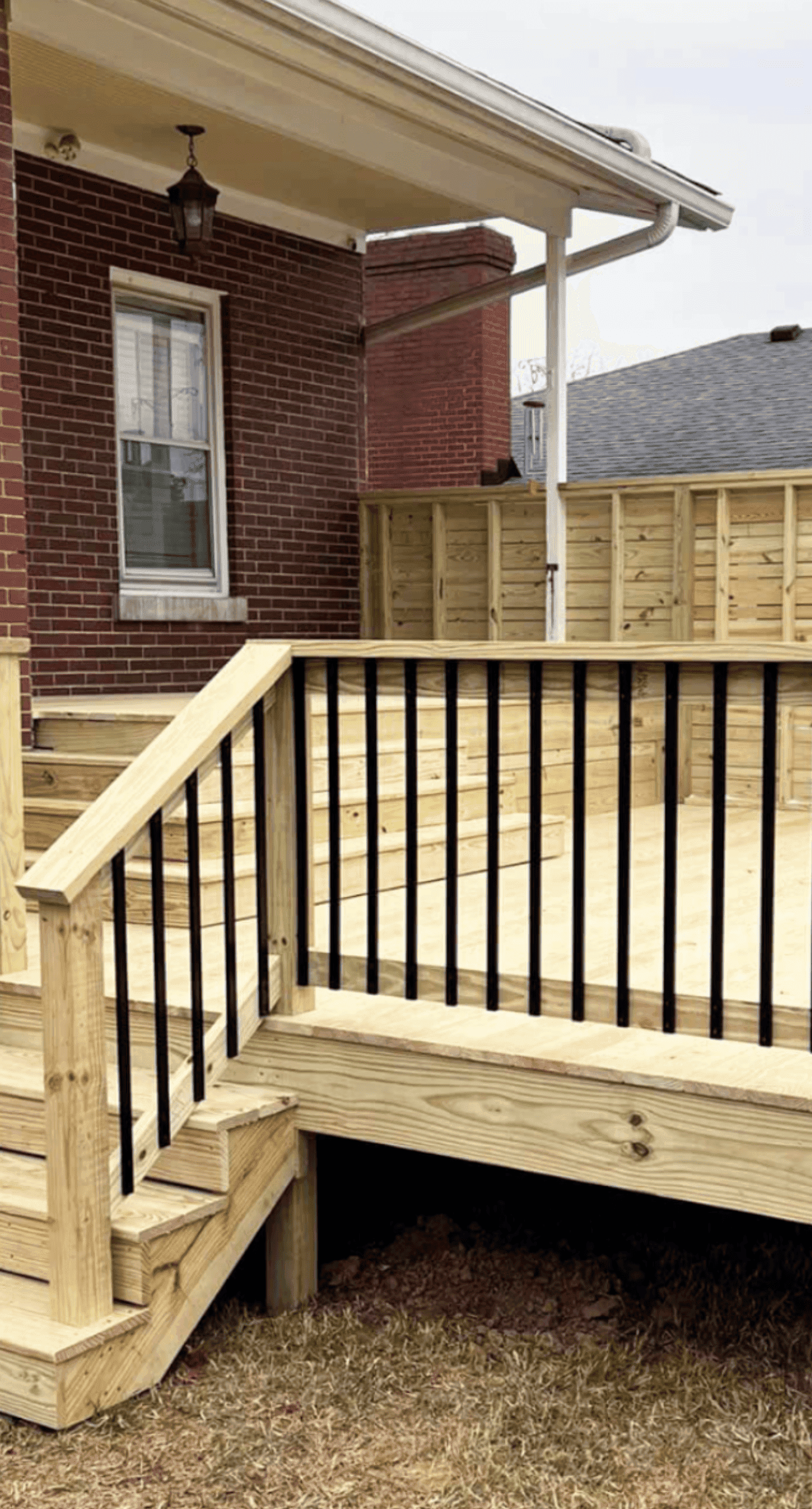 New pressure-treated deck with black metal balusters, steps and a matching privacy fence