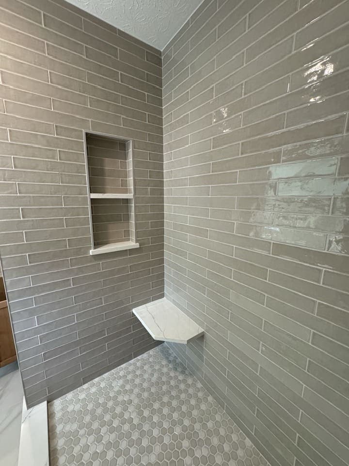 Tiled shower with a recessed niche, a corner bench and a mosaic floor