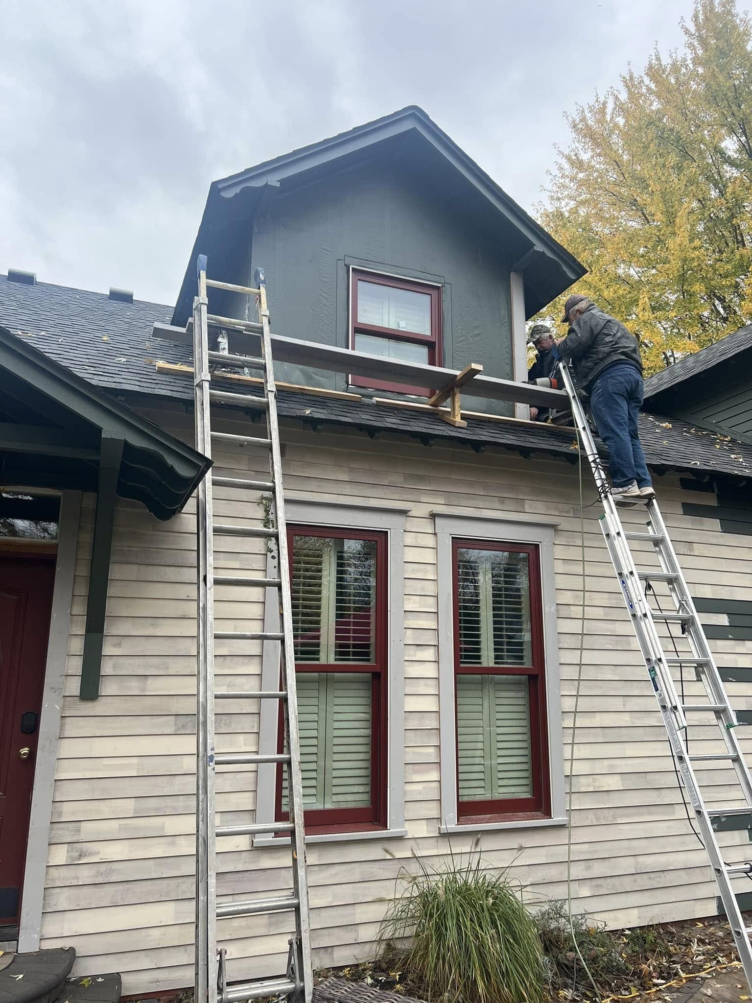 Two of the crew on ladders replacing exterior trim on a two-storey house